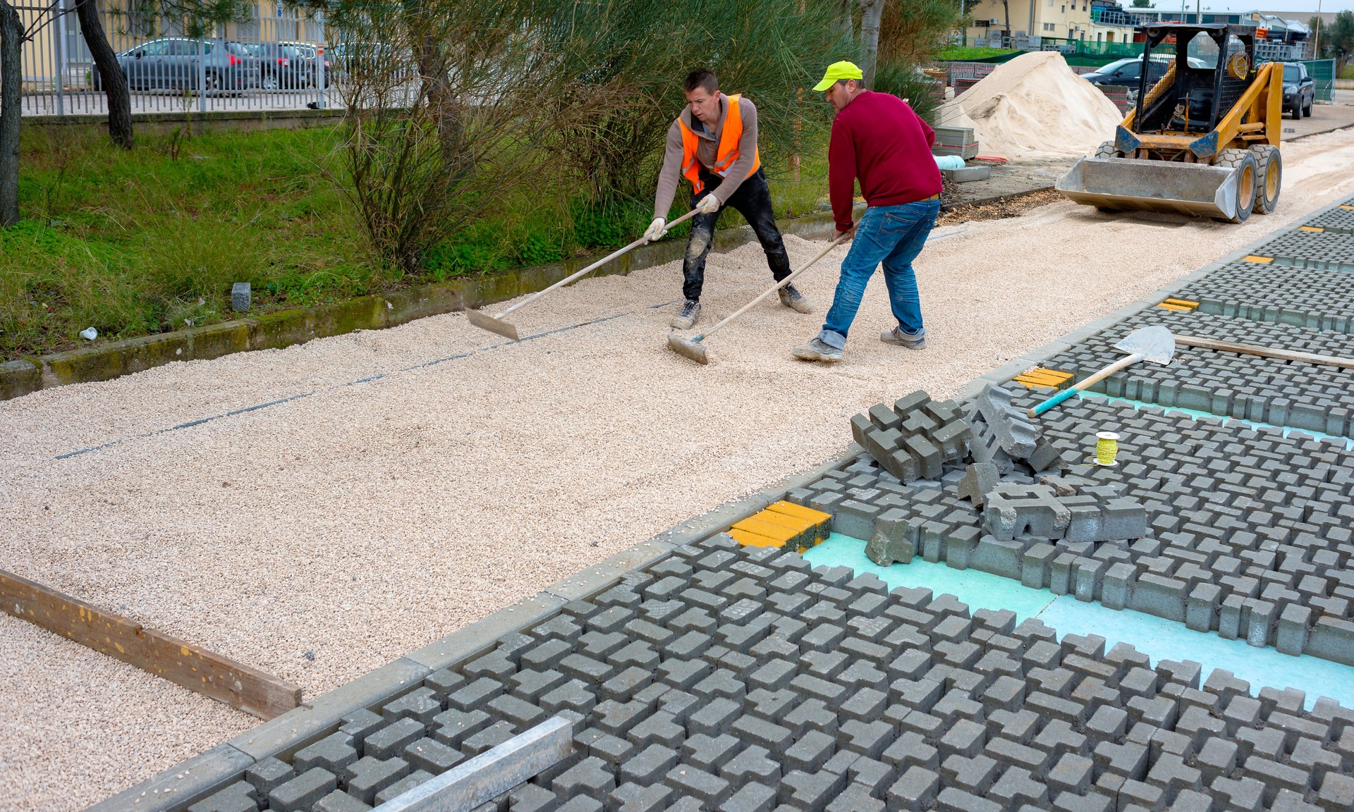 Construction worker laying interlocking paving concrete onto sheet nonwoven bedding sand and fitting them into place.